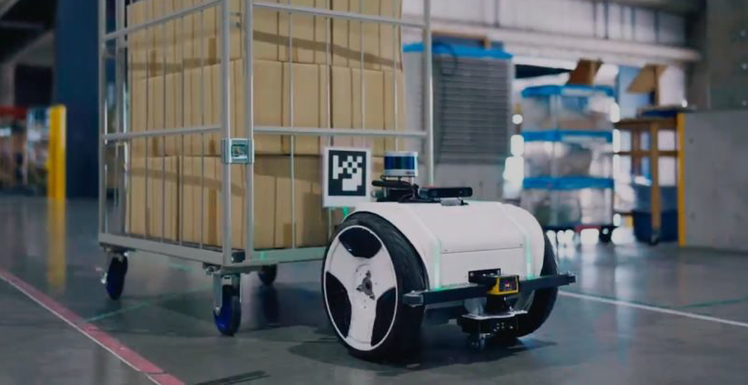 Tugbot 2 autonomous mobile robot towing a loaded cart through Tharsus’s factory, demonstrating hands-free material handling.